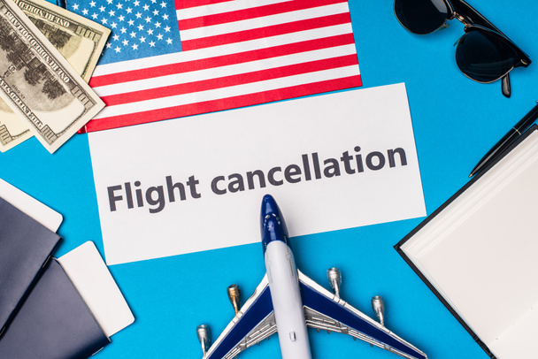 Top view of card with flight cancellation lettering near toy plane, dollars and flag of america on blue background - Foto, immagini
