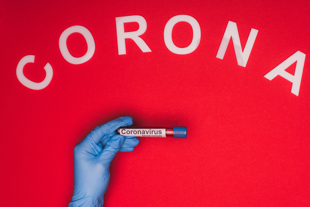 Top view of doctor holding test tube with blood sample and corona lettering on red background - Photo, Image