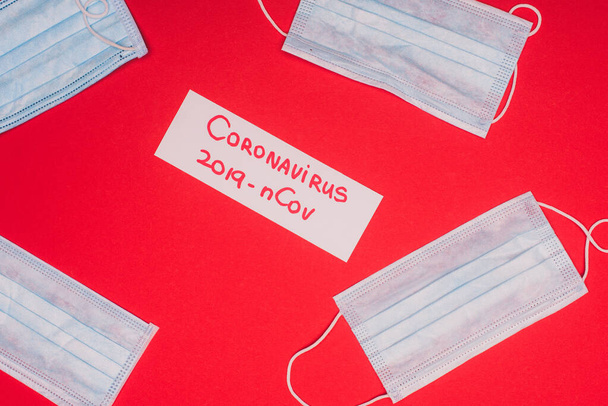 Top view of card with coronavirus 2019-nCov lettering near medical masks on red background - Photo, Image