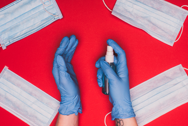 Верхний вид врача с помощью дезинфицирующего средства для рук рядом с медицинскими масками на красном фоне
 - Фото, изображение
