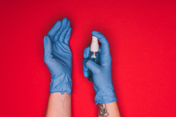 Visão superior do médico em luvas de látex segurando higienizador de mão no fundo vermelho
 - Foto, Imagem