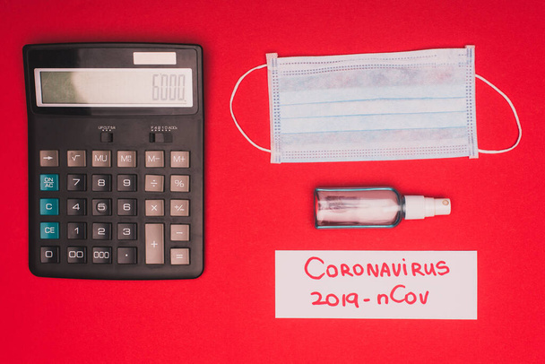 Вид зверху на медичну маску, дезінфікуючий засіб для рук з калькулятором і малюванням коронавірусу 2019-nCov на карті на червоній поверхні
 - Фото, зображення
