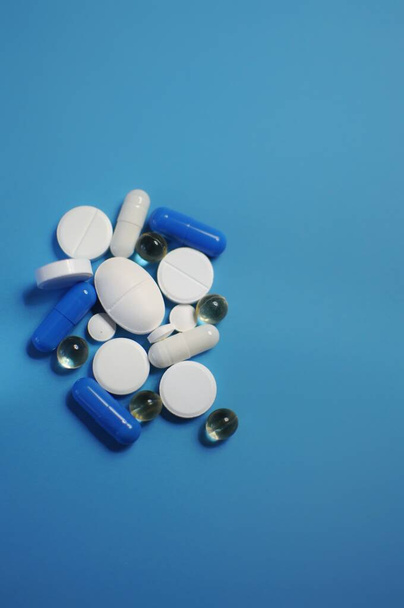 Veel verschillende pillen op de blauwe tafel. Veel kleurrijke verschillende pillen, waaronder anti-virale medicijnen. Geneesmiddelen tegen COVID-19 en andere ziekten - Foto, afbeelding