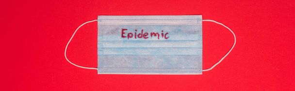 Widok z góry maski medycznej z literami epidemii na czerwonym, panoramicznym ujęciu  - Zdjęcie, obraz