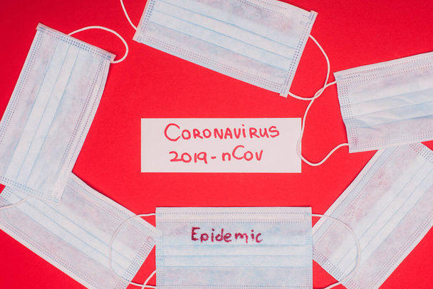 Top view of medical masks with epidemic and card with coronavirus 2019-nCov lettering on red background - Foto, Imagen