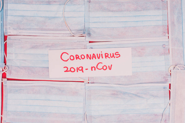 Top view of card with coronavirus 2019-nCov lettering on medical masks on red background - 写真・画像