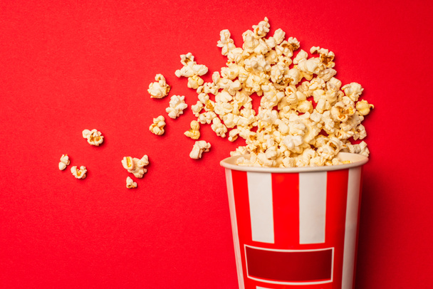 Top view of bucket with tasty popcorn on red background - Фото, изображение