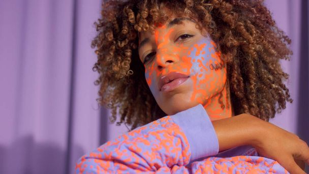 Mixed race woman with curly hair and bright neon makeup pattern on the face the same like on her sweatshirt - Photo, Image