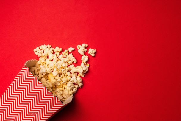 Top view of bucket with tasty popcorn on red background - 写真・画像
