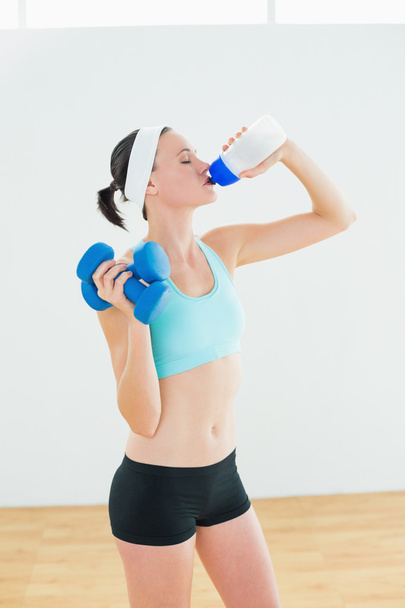 Toned woman with dumbbells drinking water - Фото, изображение