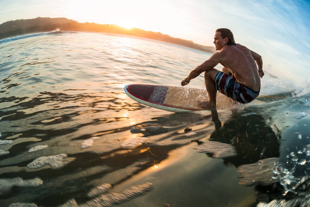 Молодой человек плывет по океанской волне на спокойном восходе солнца - Фото, изображение