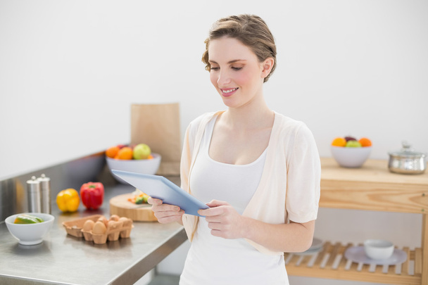 Smiling cute woman using her tablet standing in her kitchen - Photo, image
