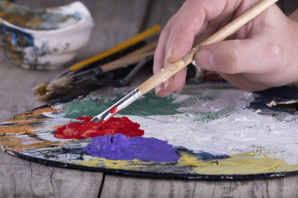 Fine art school. Closeup of wooden palette with acrylic paint and paintbrush in artist hands. - Fotografie, Obrázek