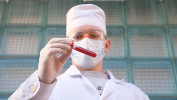 Médico jovem com luvas de proteção e óculos testa amostras de sangue no hospital. Médico homem segurando tubo de teste com amostra de sangue para coronavírus. Conceito de vida em saúde e segurança da pandemia de COVID-19
 - Filmagem, Vídeo