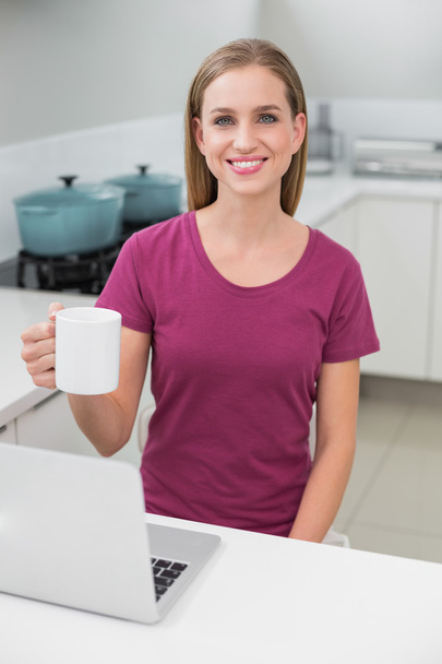 Blonde casual woman using laptop holding mug - Фото, изображение