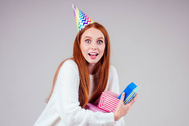 redhaired ginger woman wearing birthday cap horn holding many gift boxes in studio white background - Fotoğraf, Görsel