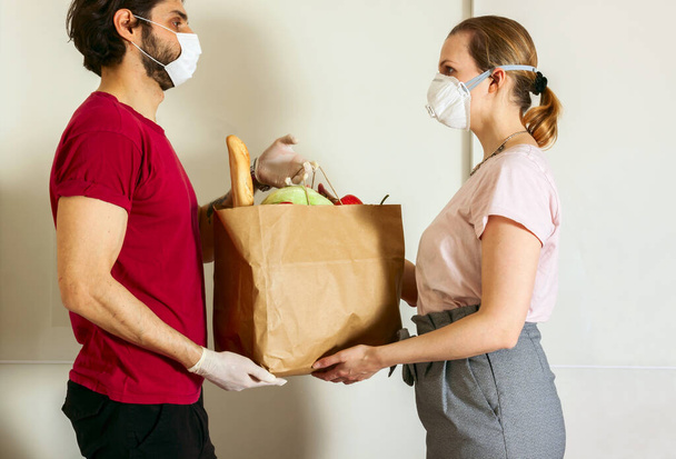 保護マスクと医療用手袋の宅配便は持ち帰り用の食品を提供します。隔離下での配送サービス,病気の発生,コロナウイルスcovid-19パンデミック  - 写真・画像