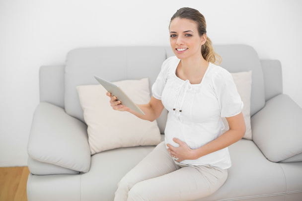 Content pregnant woman holding her tablet smiling at camera - Foto, Imagem
