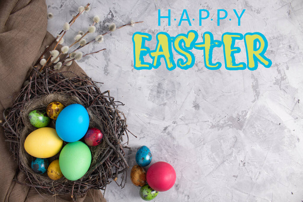 Eggs with willow branches for the holiday. Easter. Multicolored eggs in a nest on a light background. The view from the top. Copy space. Lettering Happy Easter. - Φωτογραφία, εικόνα