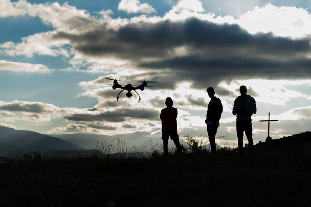  Jovenes volando un dron en un contraluz nublado al amanecer - Foto, immagini