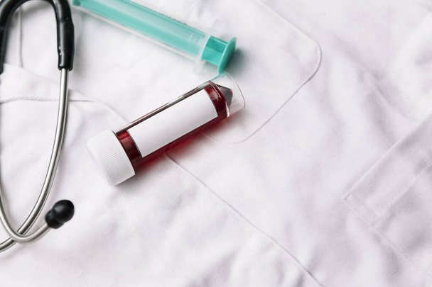 blood sample test tube with blank label with copy space for text and medical equipment on a white doctor gown, health and medicine concept, copy space for text - Foto, Imagem
