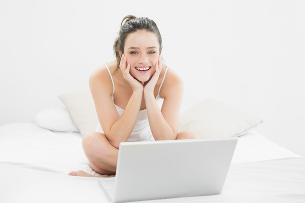 Smiling casual woman with laptop sitting on bed - Valokuva, kuva