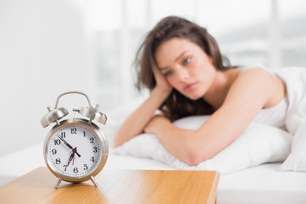 Sleepy woman looking at alarm clock on bedside table - Фото, изображение