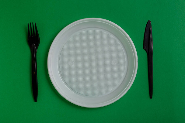 Yeşil arka planda plastik tek kullanımlık aletler. çatal, bıçak, tabak - Fotoğraf, Görsel
