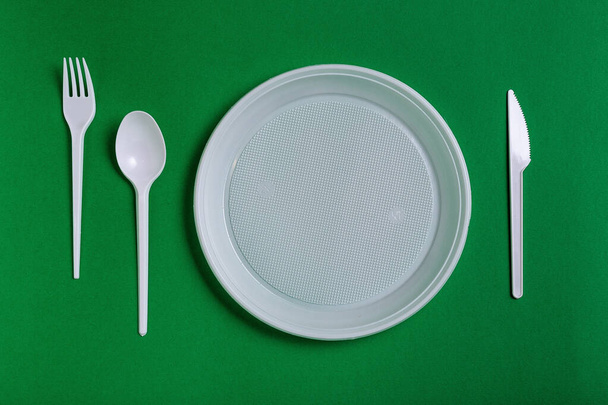 Plastic wegwerpgereedschap op groene achtergrond. vork, messen, platen - Foto, afbeelding