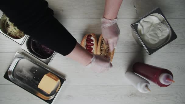 Vue du dessus des mains du chef dans des gants cuisine un hot dog, saucisse dans la pâte. Chef met du chou et des oignons marinés dans un hot dog
 - Séquence, vidéo