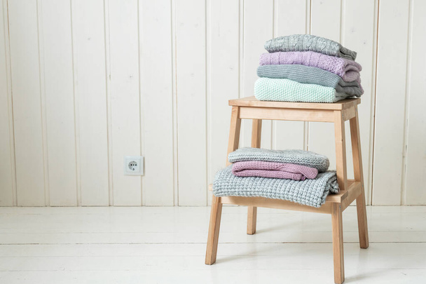 Stack of cozy knitted sweaters on a wooden ladder. Scandinavian style. White wooden wall - Foto, Bild