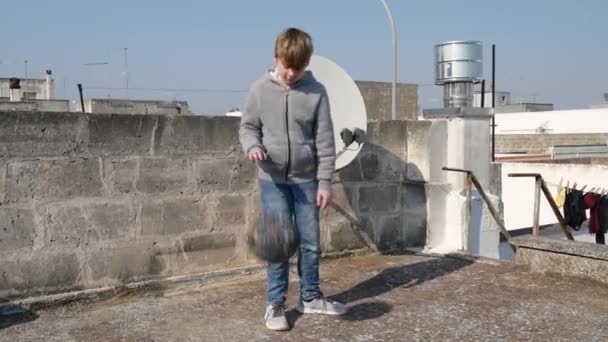 Мальчик капает мяч на крышу своего дома во время карантина коронавируса ковид-19. Детская корзина для здоровья. Идея деятельности детей домашние тренировки, карантинный спорт
 - Кадры, видео