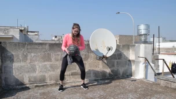 Thuis geïsoleerd. Jong meisje sport op het dak van haar huis tijdens quarantaine. Vrouwelijke fitnesstraining in sportkleding. Begrip sport en gezondheid. Quarantainesport thuis - Video