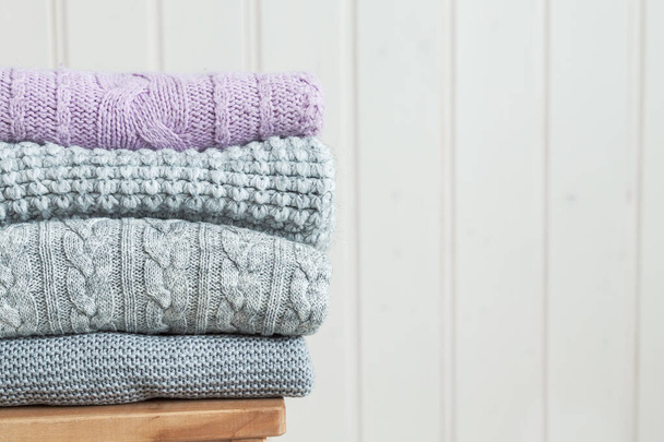 Stack of cozy knitted clothes on a wooden ladder. Scandinavian style. White wooden wall - Photo, image