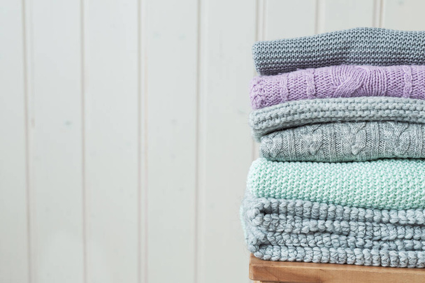 Stack of cozy knitted sweaters on a wooden ladder. Scandinavian style. White wooden wall - Fotografie, Obrázek
