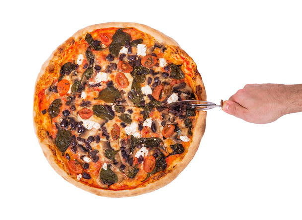 The chef cuts the pizza with a pizza cutter, top view. Tasty pizza with mozzarella, feta, cherry tomatoes, spinach, mushrooms and kalamata olive, isolated on white background with clipping path - Photo, Image