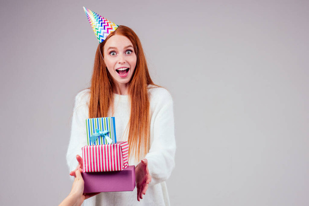 Kızıl saçlı, kızıl saçlı, doğum günü şapkalı kadın elinde stüdyo beyaz arka planda bir sürü hediye kutusu tutuyor. - Fotoğraf, Görsel