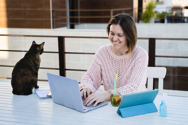 Female working remotely at home terrace with her pet - Фото, изображение
