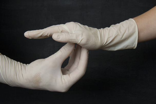 Ruce v lékařských bílých gumových rukavicích na černém pozadí. Ochranné jednorázové rukavice chrání před viry, koronaviry, nebezpečnými bakteriemi. - Fotografie, Obrázek