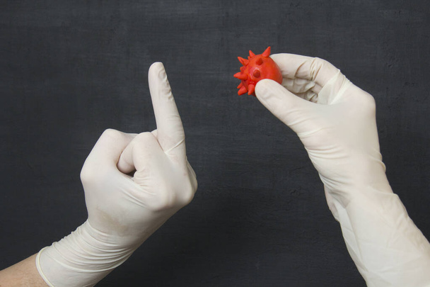 Mão em branco médica luva de látex de borracha descartável mostra dedo médio para coronavírus vermelho em outra luva de borracha. Vai-te foder. Luvas descartáveis protetoras proteger contra vírus, coronavírus
. - Foto, Imagem