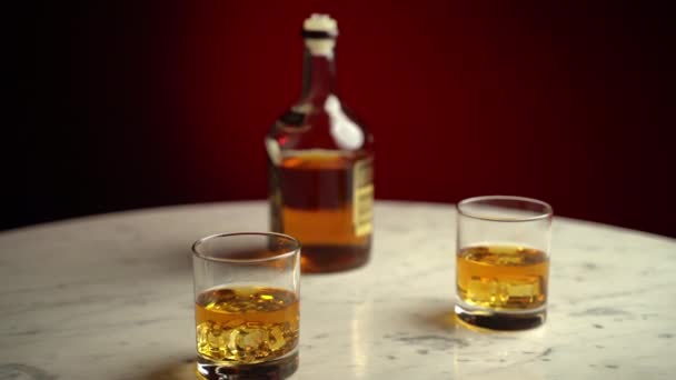 Zlatý originální whisky nápoj s kostkami ledu v křišťálově čistých sklenicích na mramorovém stole, oslavou nočního života a alkoholickým odpočinkem. Zlatý koňak ve skle, jezdec ve 4K - Záběry, video