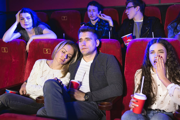 Young people watching a boring movie at the cinema, girl is sleeping. - Фото, зображення