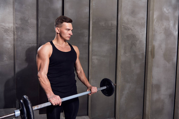 man in black sports uniform with dumbbells on a background of gray wall - Fotografie, Obrázek