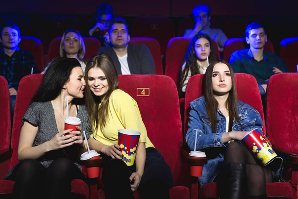Молоді жінки дивляться фільм у кінотеатрі, сміються, розмовляють, їдять попкорн і п'ють Колу. - Фото, зображення