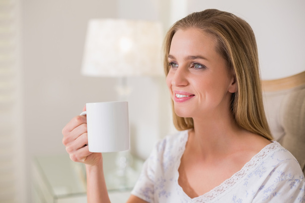 Natural happy woman sitting on bed holding mug - 写真・画像