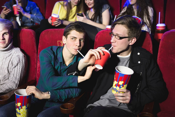 Δύο φίλοι, αδέλφια πίνουν μέσα από ένα σωλήνα στον κινηματογράφο. - Φωτογραφία, εικόνα