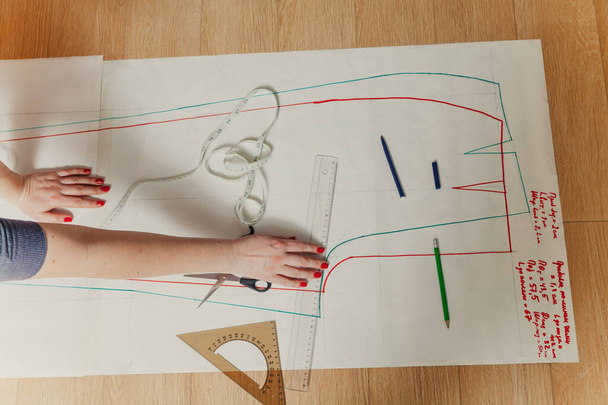 Designer creates a model. Female hands with a manicure do the layout of the sewing pattern on pape - Фото, зображення