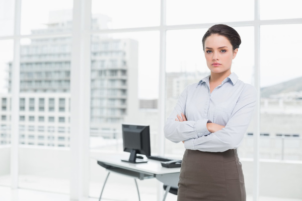 Elegant businesswoman standing with arms crossed in office - 写真・画像