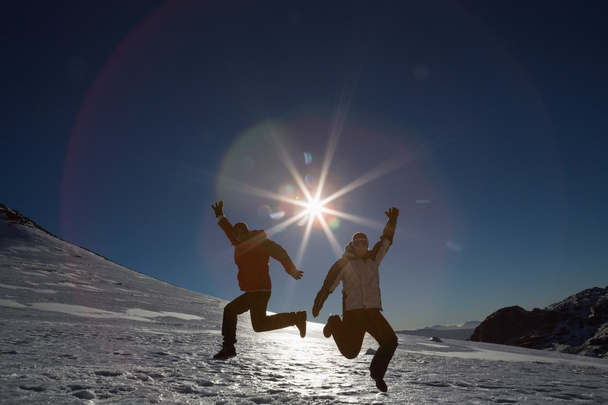 Silhouette couple jumping on snow against sun and blue sky - Fotó, kép