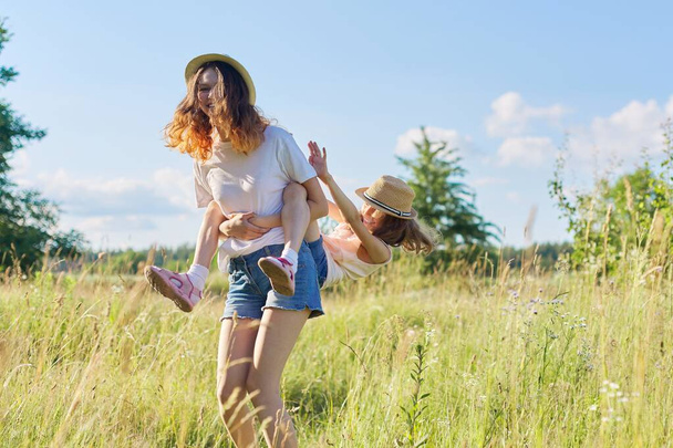 Happy children two girls sisters teenager and younger laughing and having fun in meadow, blue sky, summer nature. Active healthy lifestyle, friendly family, happy childhood, copy space - Foto, immagini